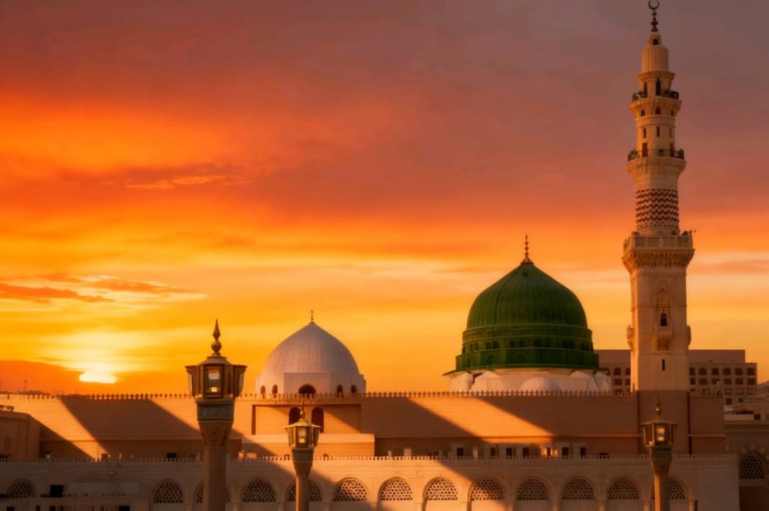 Sunset over a mosque courtyard with a prominent green dome and tall ornate minaret silhouetted against an orange sky.