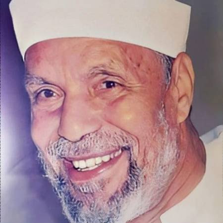 Close-up of an older man wearing a white cap, smiling broadly with a grey beard and warm eyes