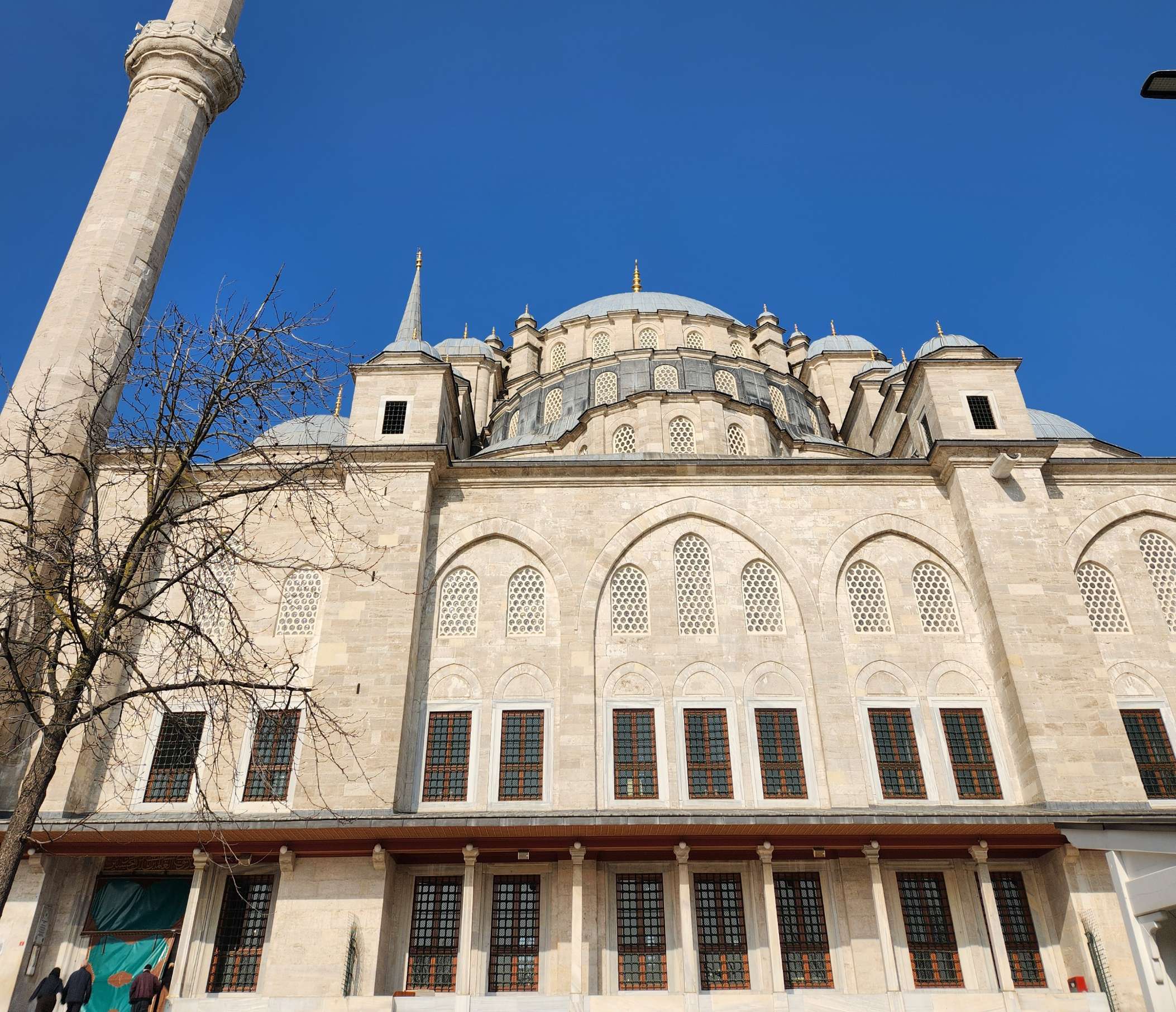 Large stone mosque facade with arched windows, ornate dome and minaret against a clear blue sky.