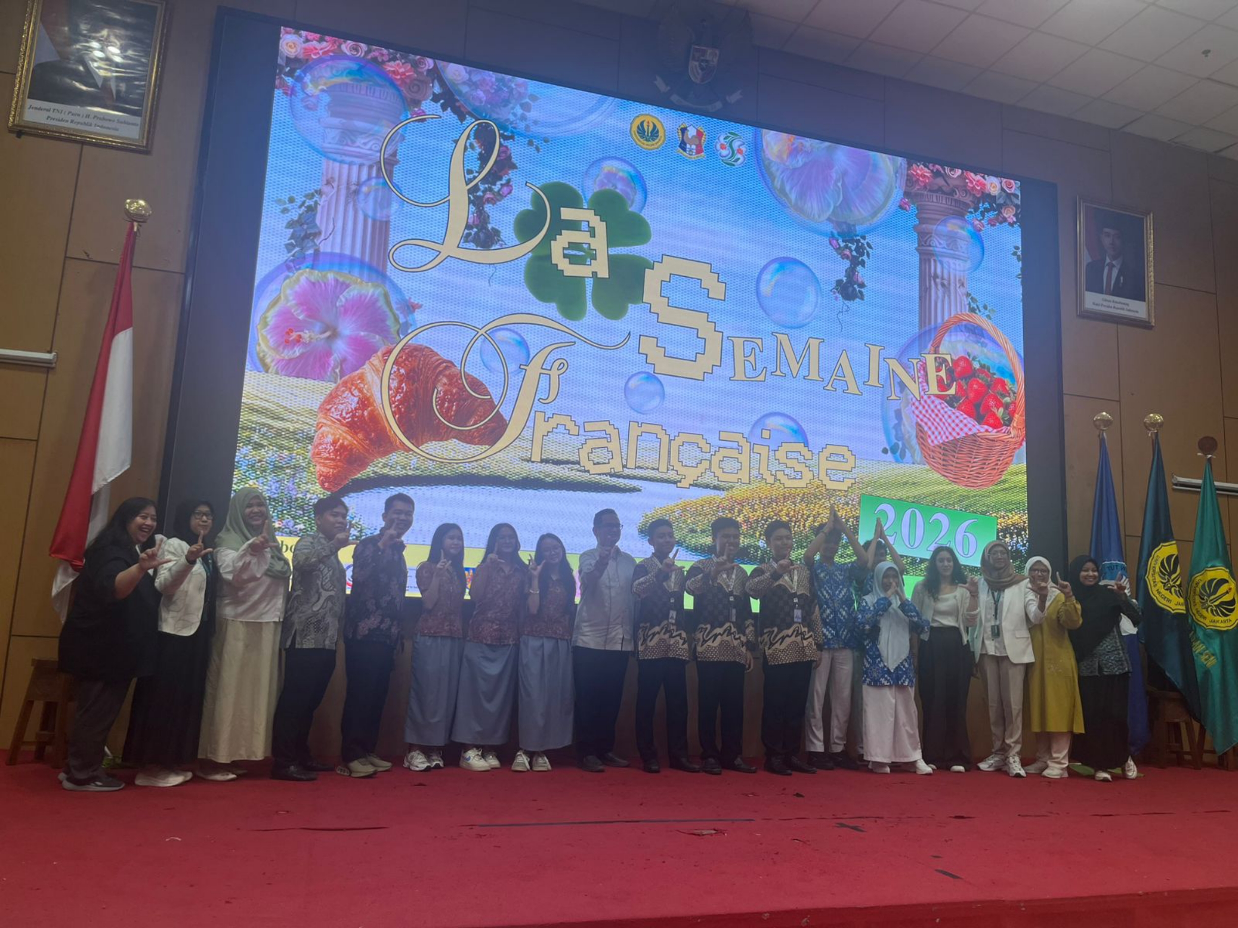 Group of students and teachers standing on stage in front of a colourful "Le Semaine Française 2026" event backdrop