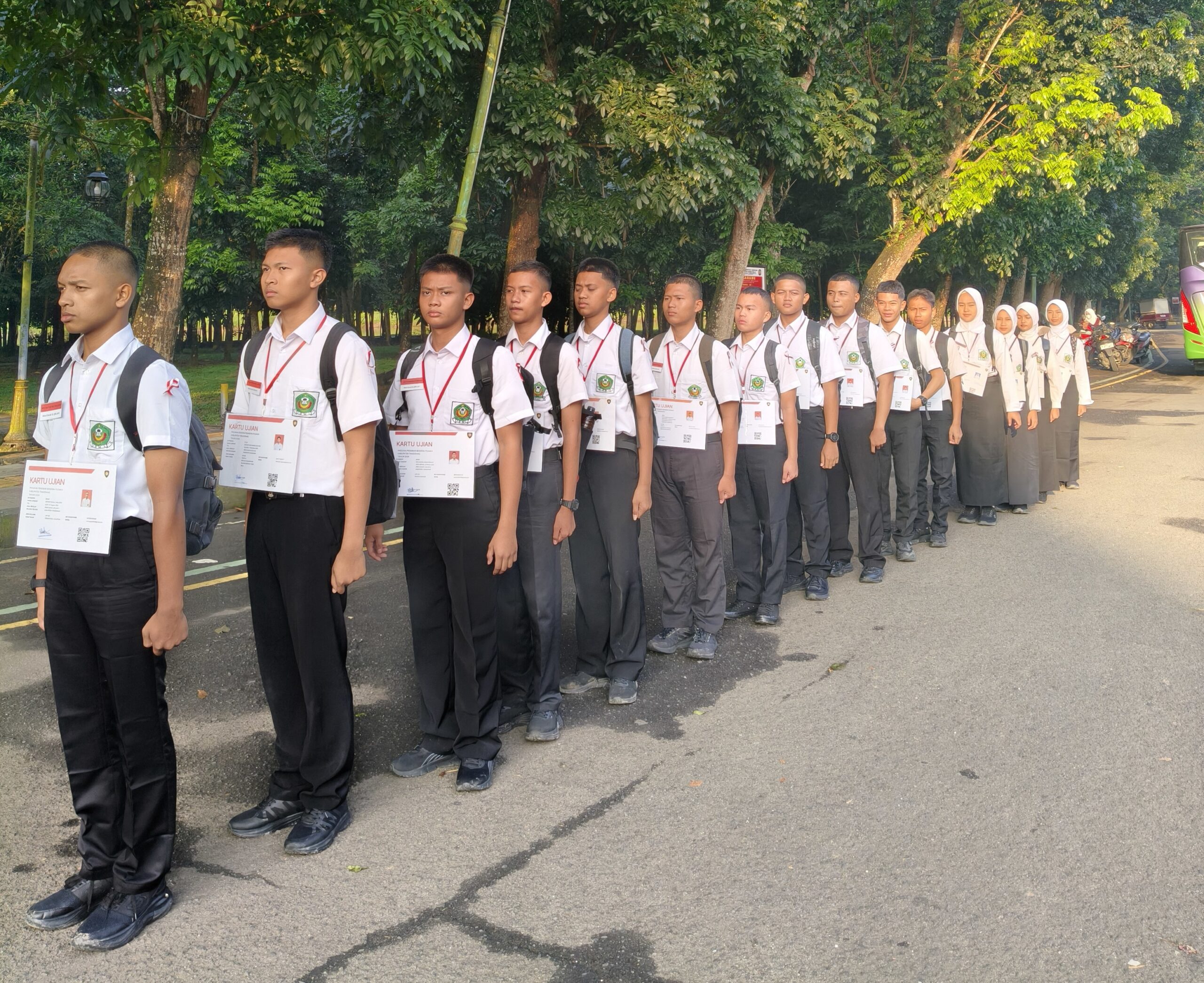 Line of high-school students in white shirts and black trousers or skirts, standing in formation outdoors with ID cards hanging from red lanyards.