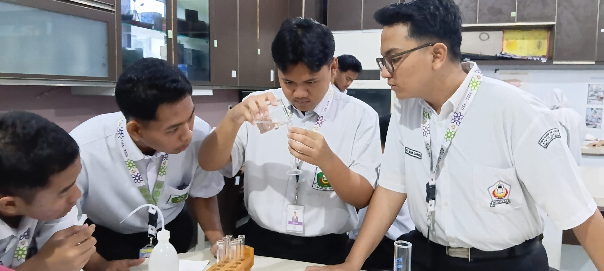 Four male students in white uniforms concentrating as one pours liquid into a test tube in a school lab.