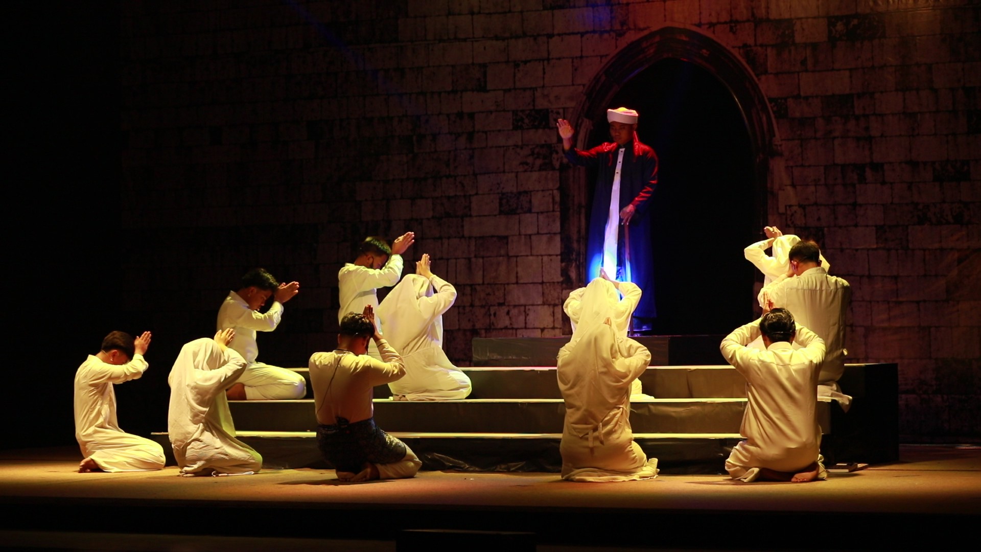 Group of kneeling worshippers in white robes facing a robed leader standing in an arched doorway bathed in blue light