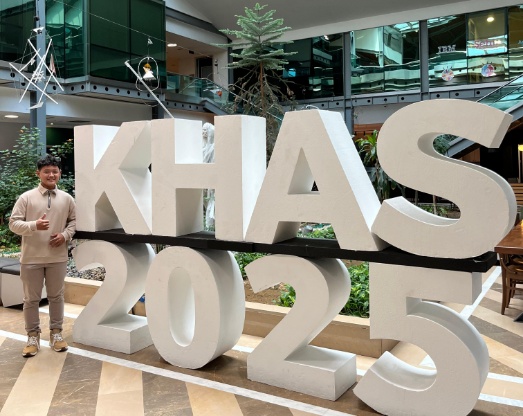 Man standing beside large white freestanding letters and numbers reading KHAS 2025 inside a modern atrium.