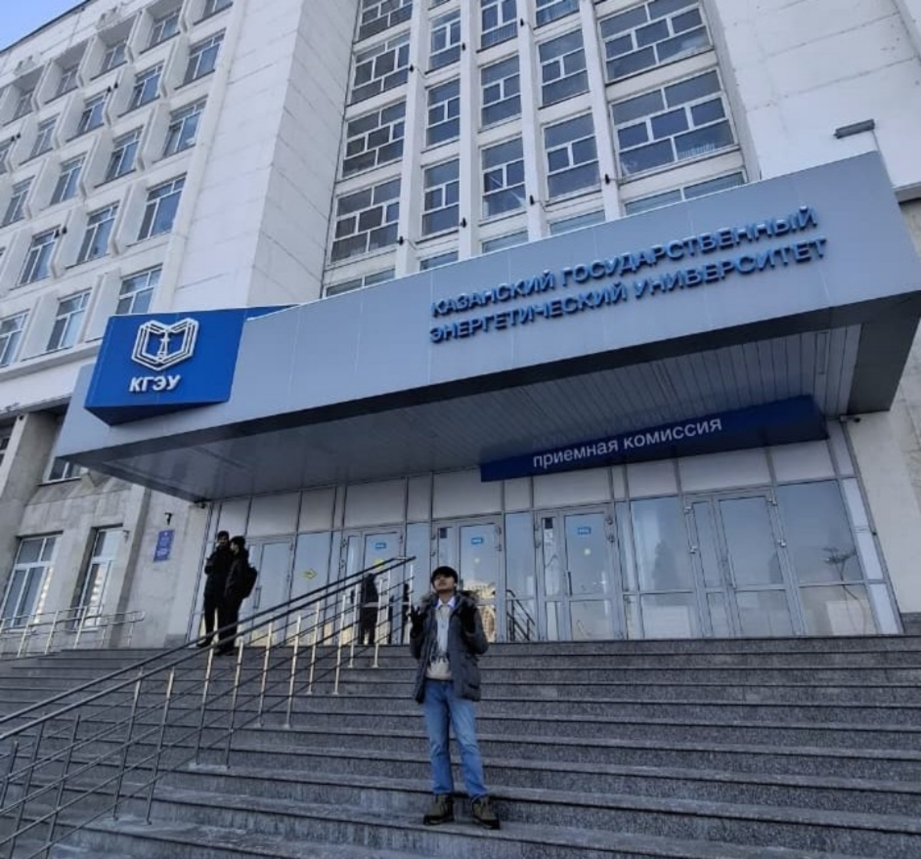 Student standing on wide stone steps leading to a modern university entrance with blue signage in Russian above the doors