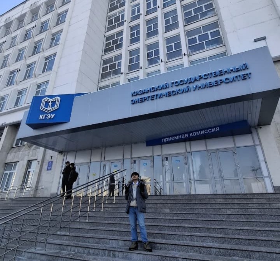 Person standing on wide stone steps outside a large multi-storey university building with blue signage in Russian above the entrance.